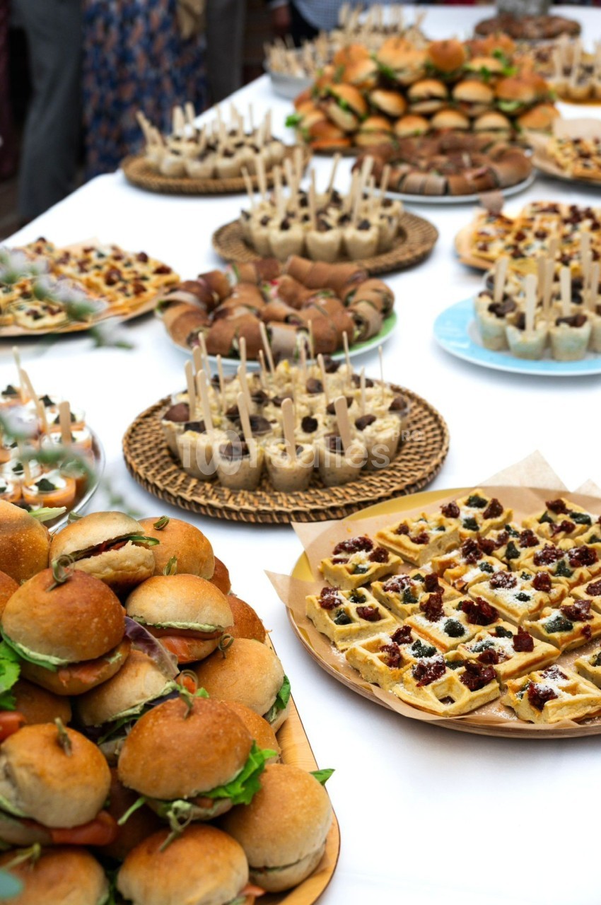 Buffet varié avec mini-burgers, gaufres garnies et amuse-bouches sur une table blanche.