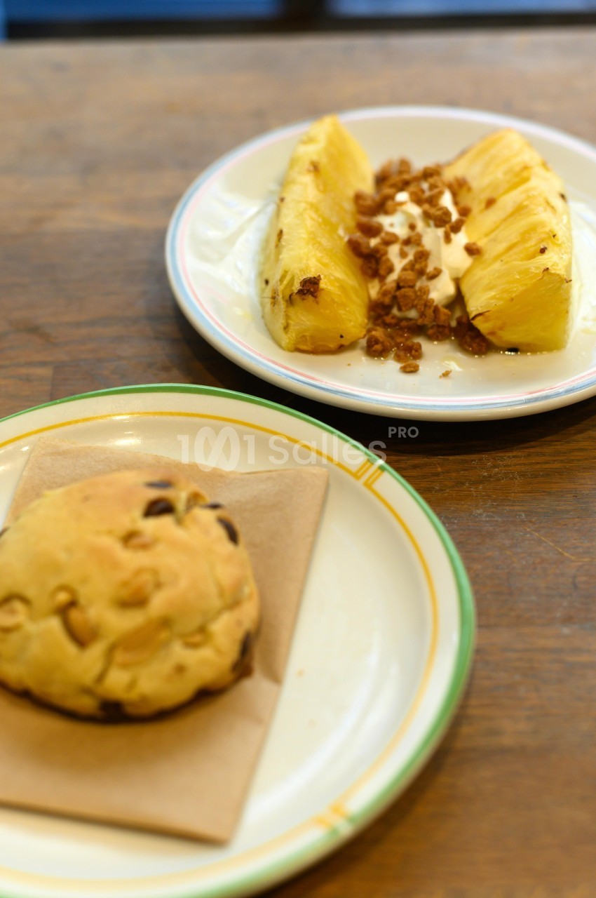 Assiette avec des tranches d'ananas, crème et granola, et une autre avec un cookie aux pépites de chocolat.
