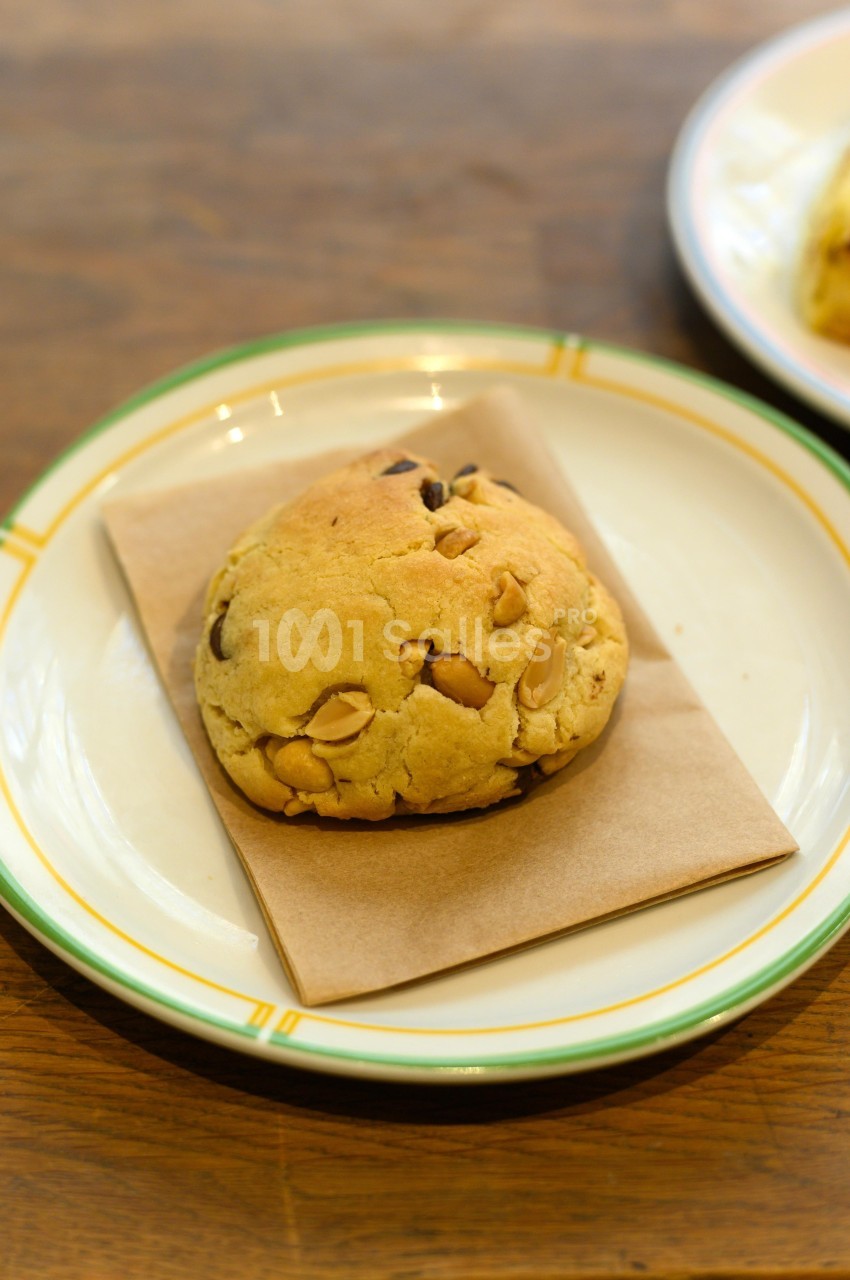 Cookie aux pépites de chocolat et noix, posé sur une serviette en papier dans une assiette blanche bordée de vert.