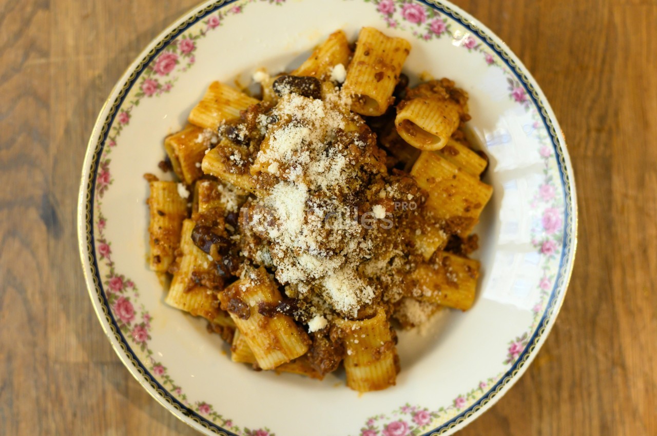 Assiette de rigatoni garnis d'une sauce tomate à la viande et saupoudrés de fromage râpé, servie sur une table en bois.
