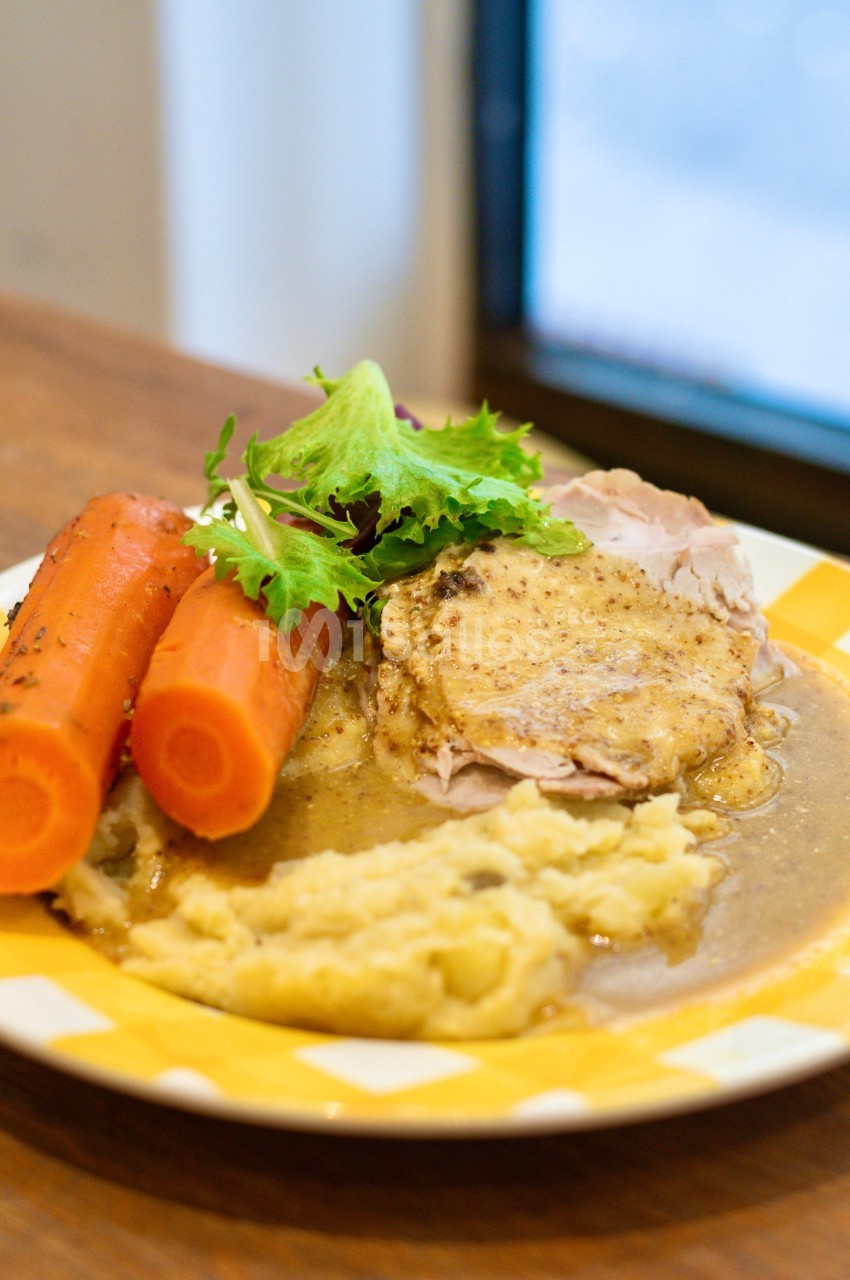 Assiette contenant de la purée, des carottes, des tranches de viande en sauce et une garniture de salade verte.