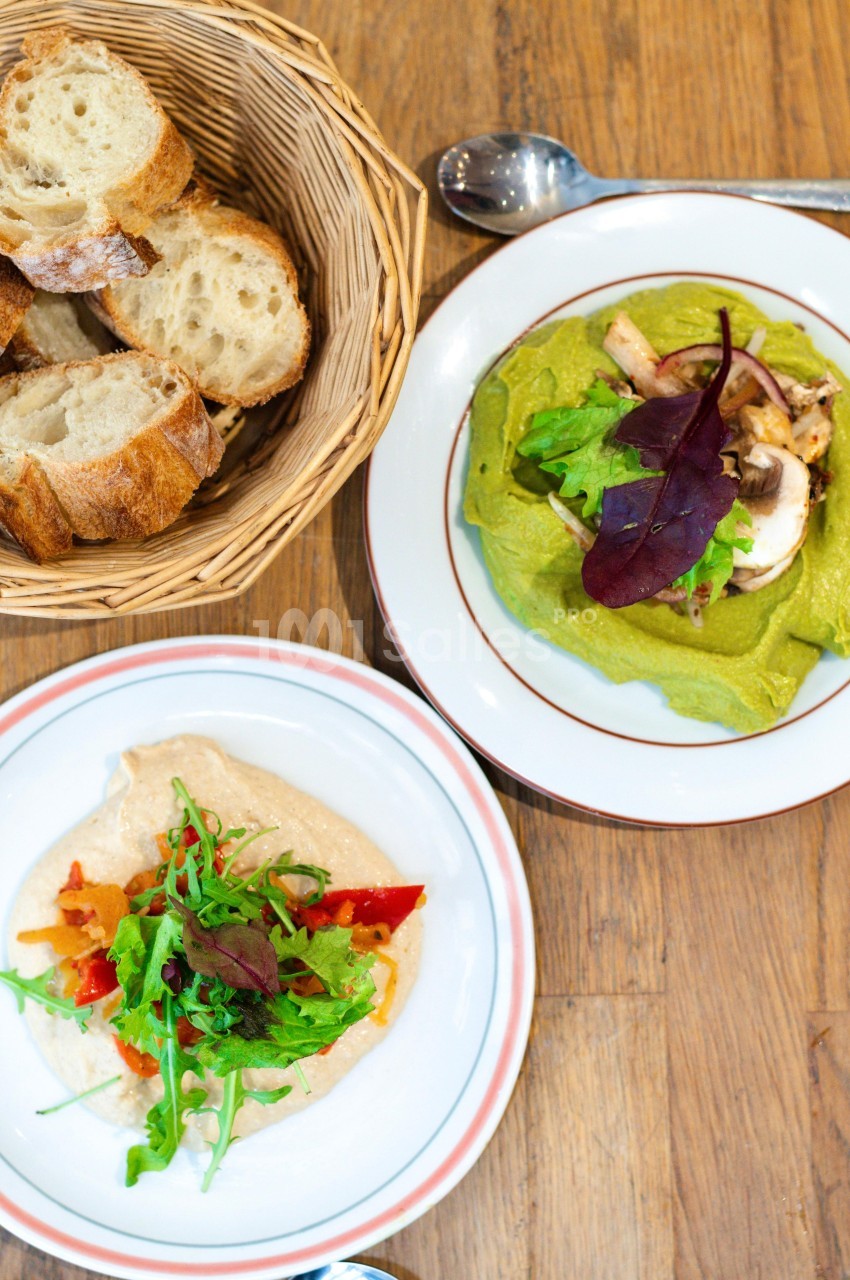 Assiettes de tartines garnies de légumes et salade, accompagnées d'un panier de tranches de pain sur une table en bois.