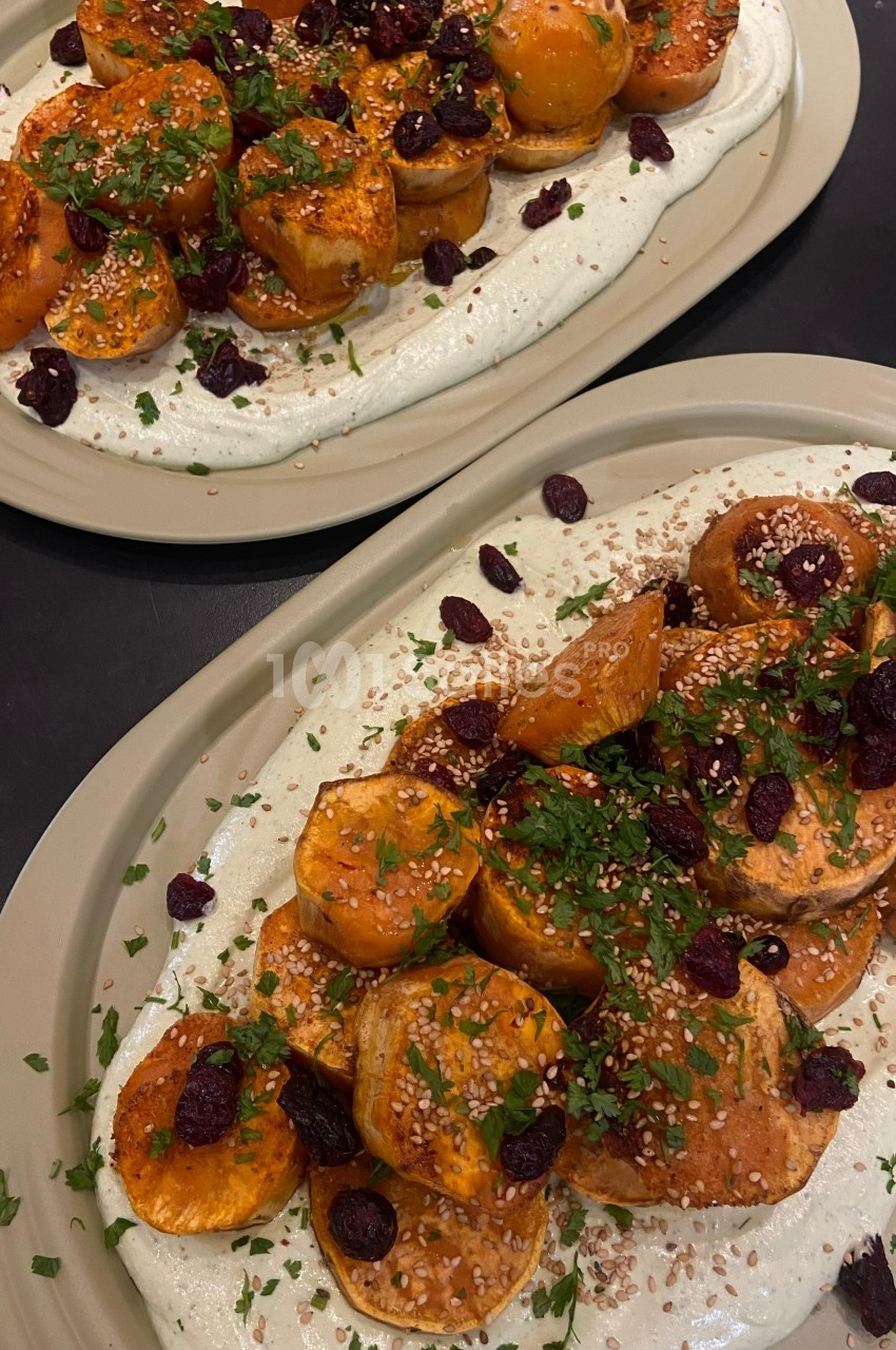 Assiette de légumes rôtis garnis de graines de sésame, herbes fraîches et cranberries sur une base crémeuse blanche.