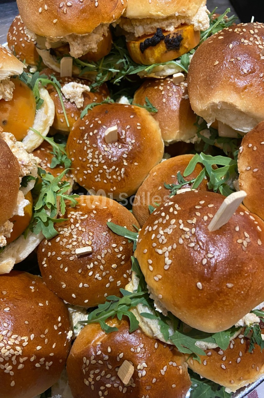 Plateau de mini-burgers garnis de roquette, fromage et autres ingrédients, avec pains briochés aux graines de sésame.