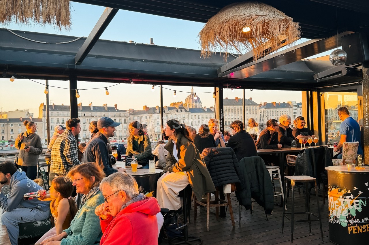 Groupe de personnes discutant et partageant un moment convivial sur une terrasse ensoleillée avec vue sur des bâtiments.