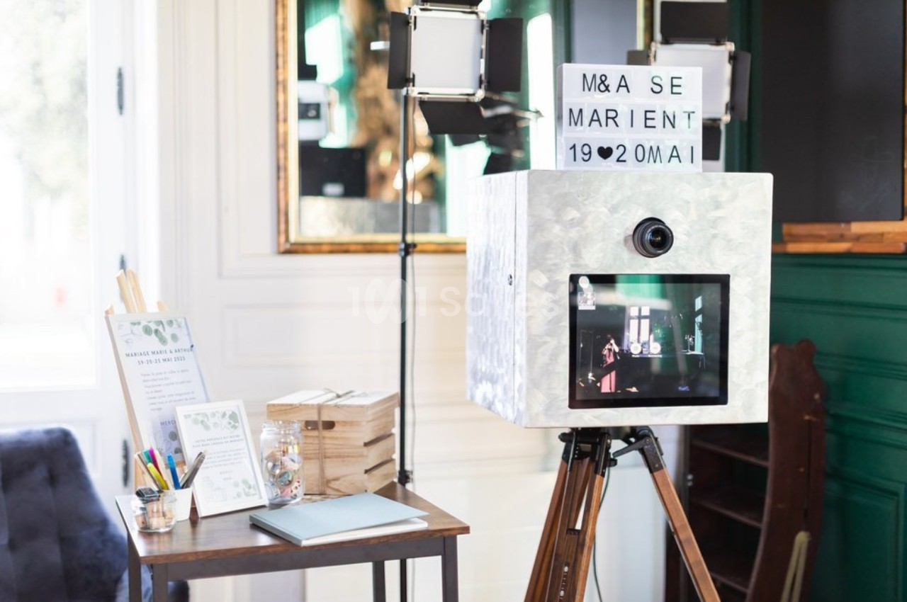 Borne photo rétro sur trépied avec écran et panneau lumineux, entourée de décorations et accessoires de mariage.
