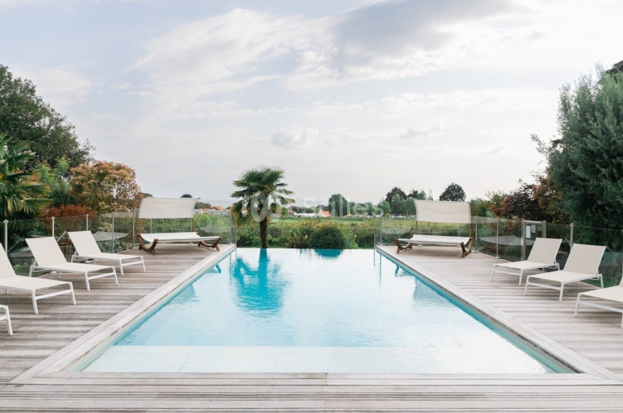 Piscine extérieure entourée de chaises longues et de végétation, avec vue sur un paysage verdoyant.