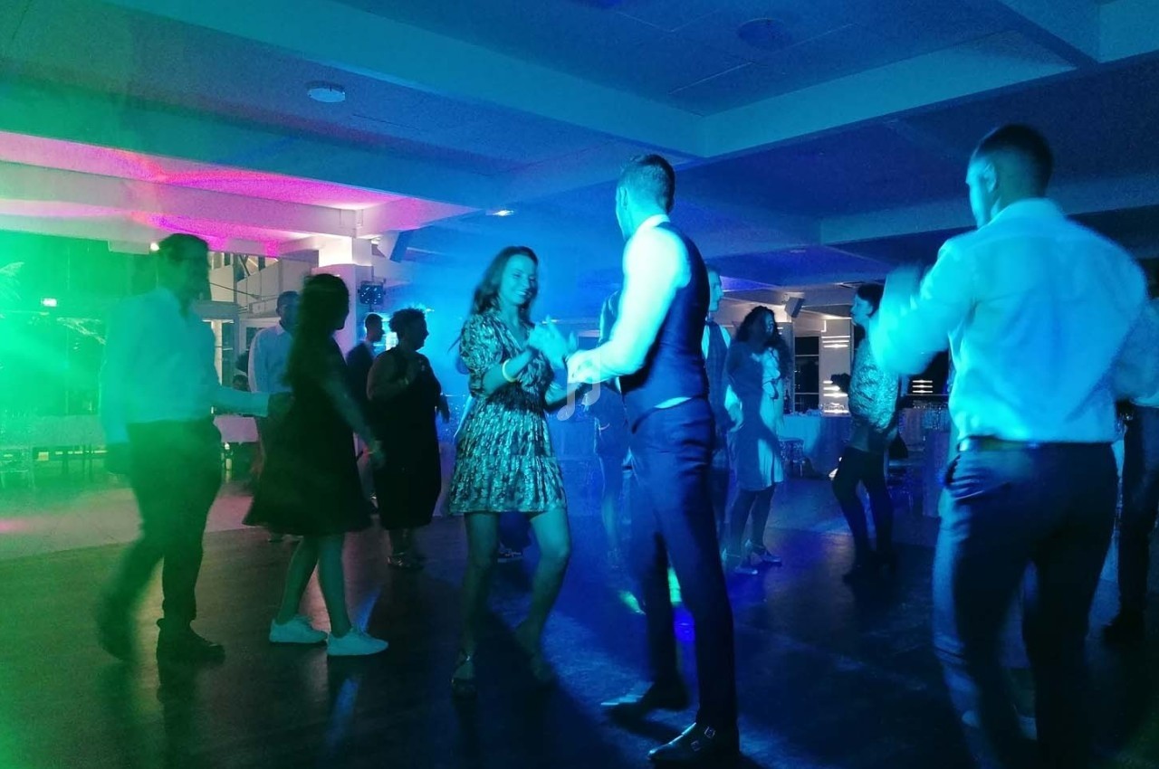 Des personnes dansent dans une salle éclairée par des lumières colorées, créant une ambiance festive.