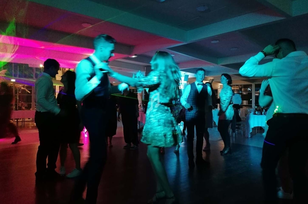 Des personnes dansent sous des lumières colorées dans une salle sombre lors d'un événement festif.
