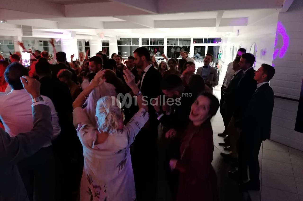 Groupe de personnes dansant et célébrant dans une salle éclairée, ambiance festive en soirée.