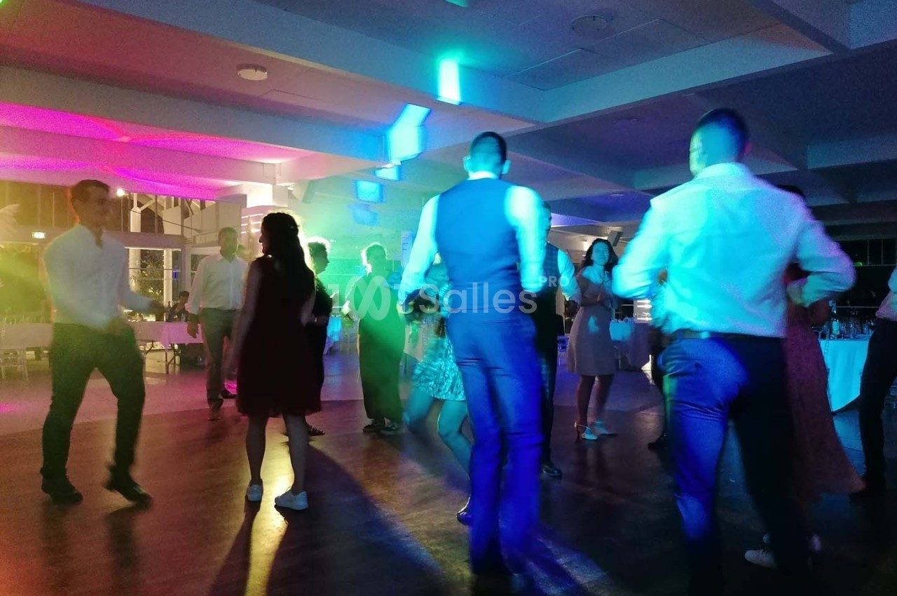 Personnes dansant sous des lumières colorées dans une salle de réception en soirée.