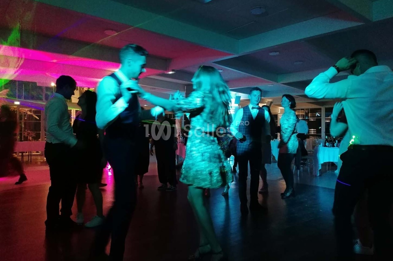 Des personnes dansent dans une salle éclairée par des lumières colorées lors d'une fête ou d'un événement.