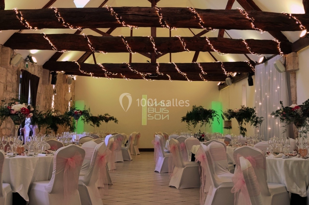 Salle de réception décorée avec des tables dressées, des chaises blanches ornées de rubans roses et des guirlandes…