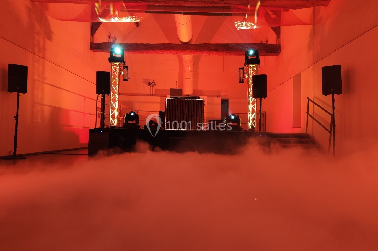 Salle de réception éclairée en rouge avec une scène équipée de matériel audio et un sol recouvert de fumée.