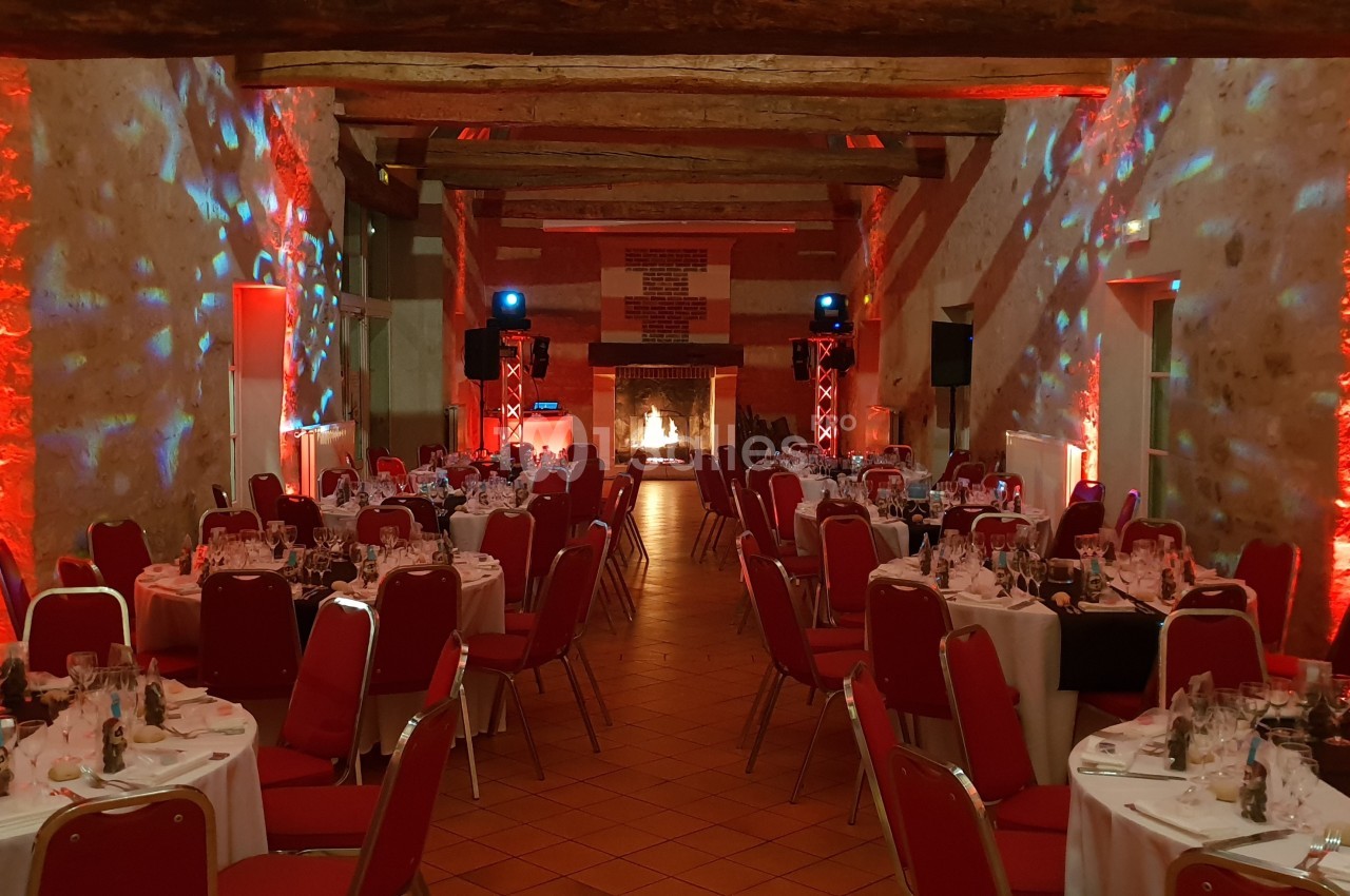 Salle de réception décorée avec des lumières rouges, tables rondes dressées et chaises rouges alignées.