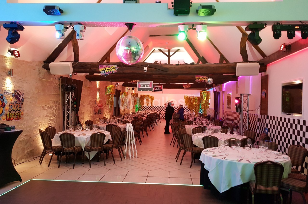 Salle décorée sur le thème des années 80 avec tables dressées, éclairages colorés et éléments rétro.