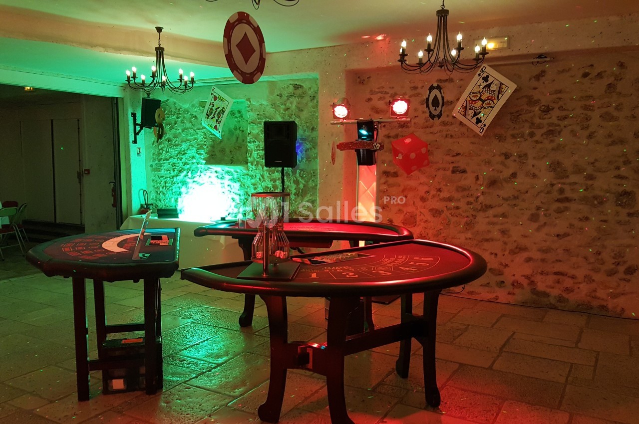Tables de jeux de casino installées dans une salle en pierre éclairée par des lumières colorées et des chandeliers.