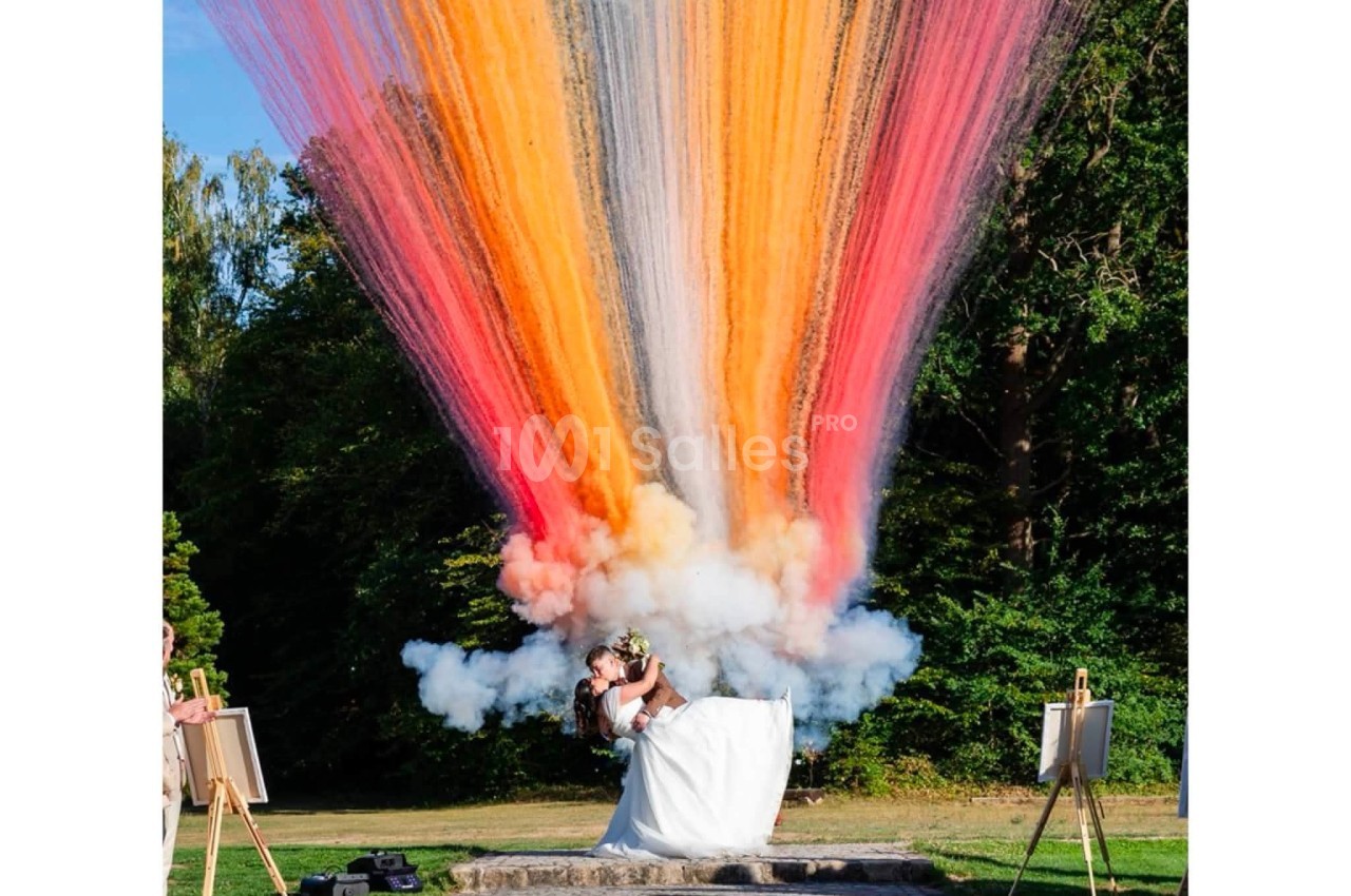 Couple en tenue de mariés créant une explosion de poudre colorée multicolore en extérieur.