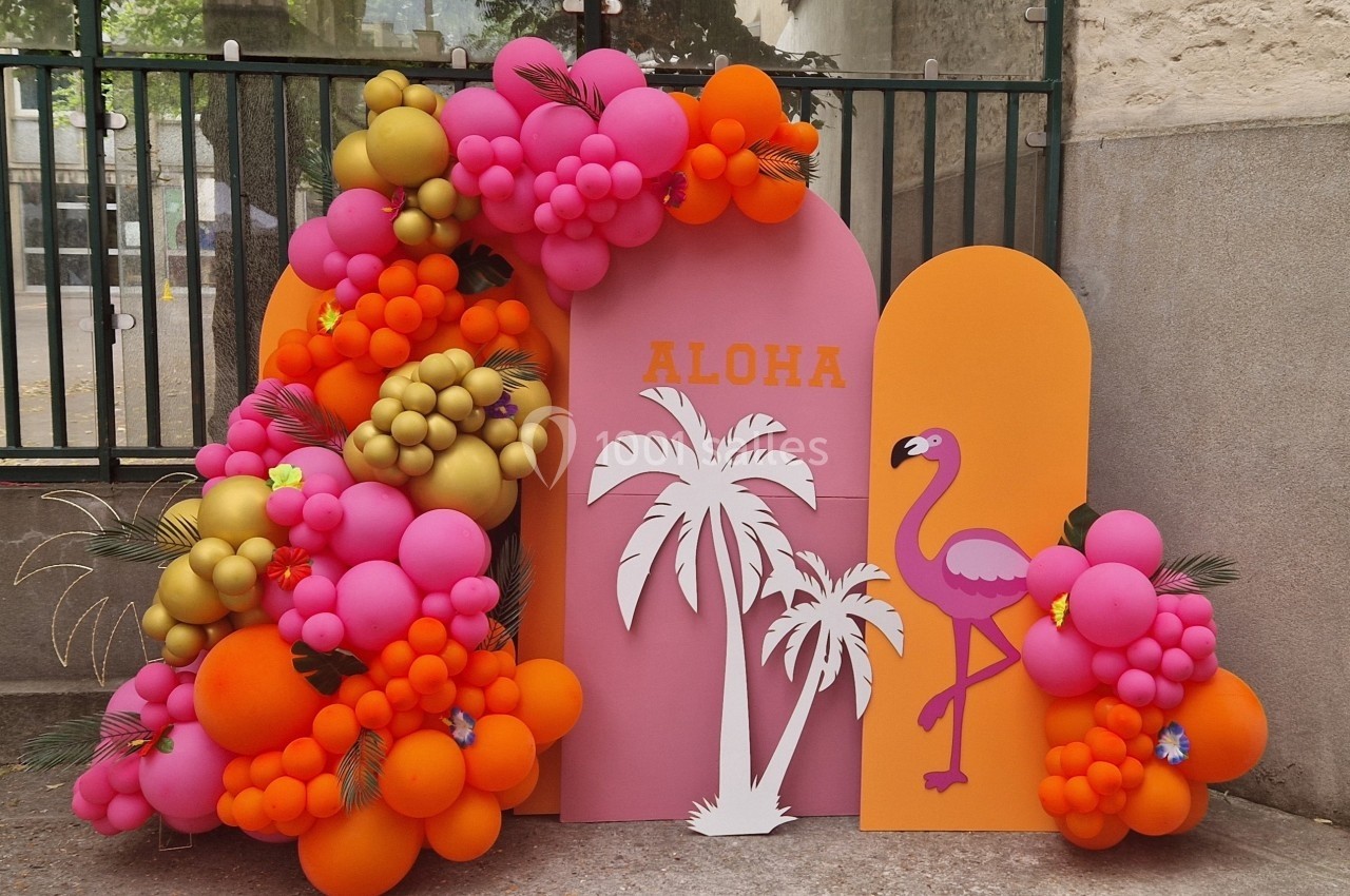 Décor tropical avec ballons colorés, flamant rose, palmiers et inscription ’Aloha’ sur des panneaux roses et orange.