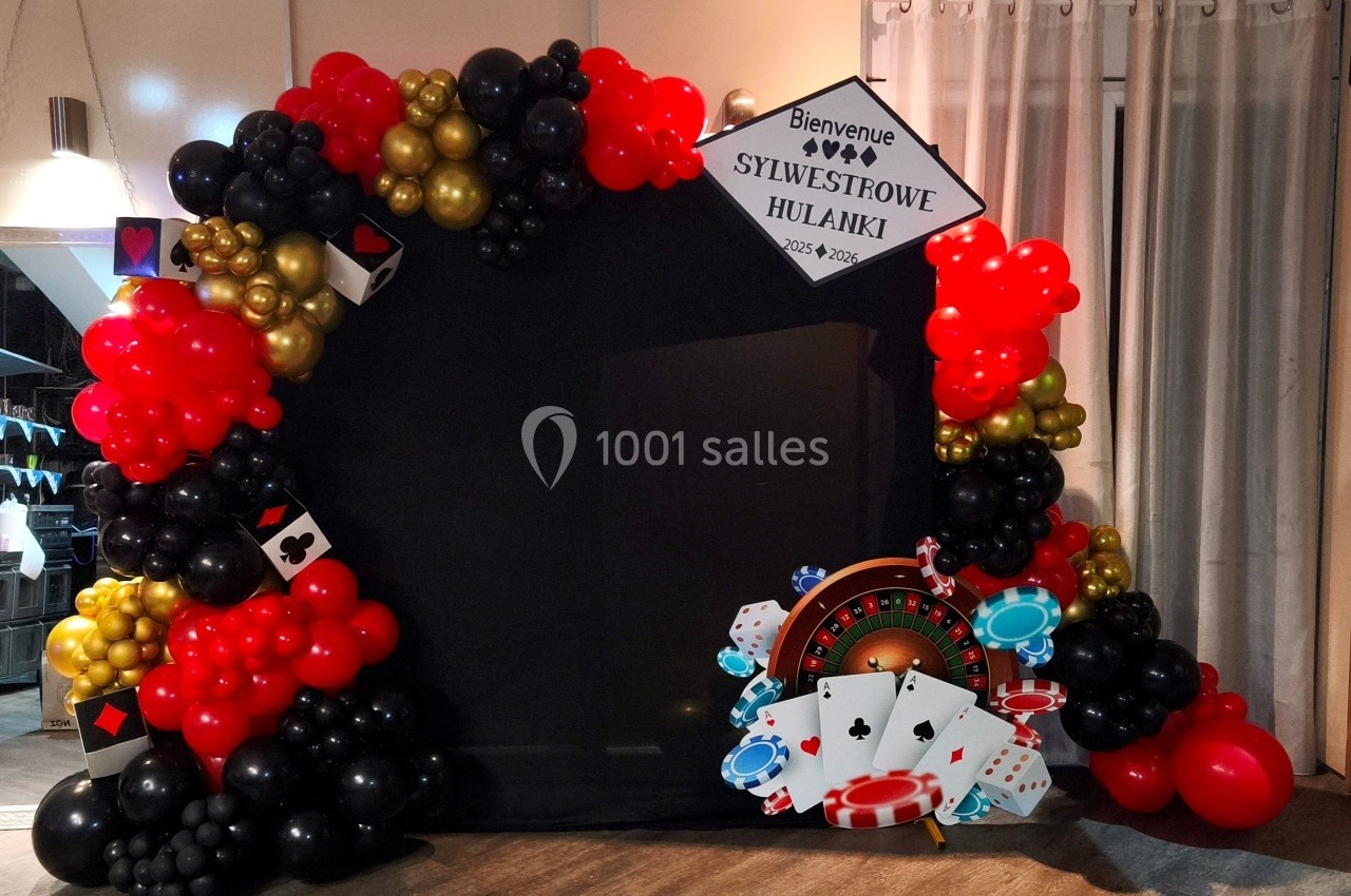 Arc de ballons rouges, noirs et dorés décoré sur le thème du casino, avec cartes et jetons en bas.