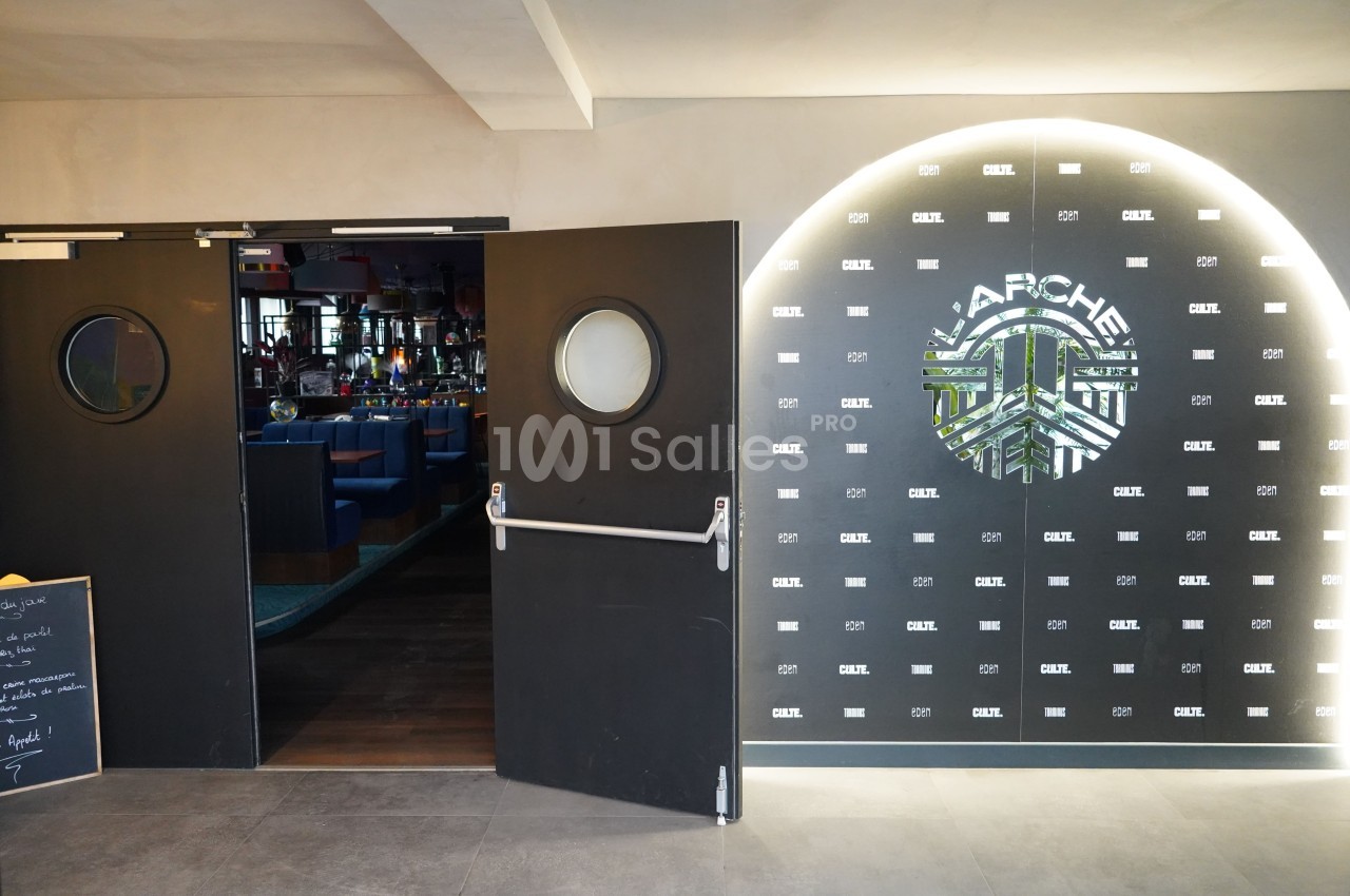 Entrée d'un restaurant avec portes battantes noires et mur décoratif éclairé affichant le logo ’Apache’.