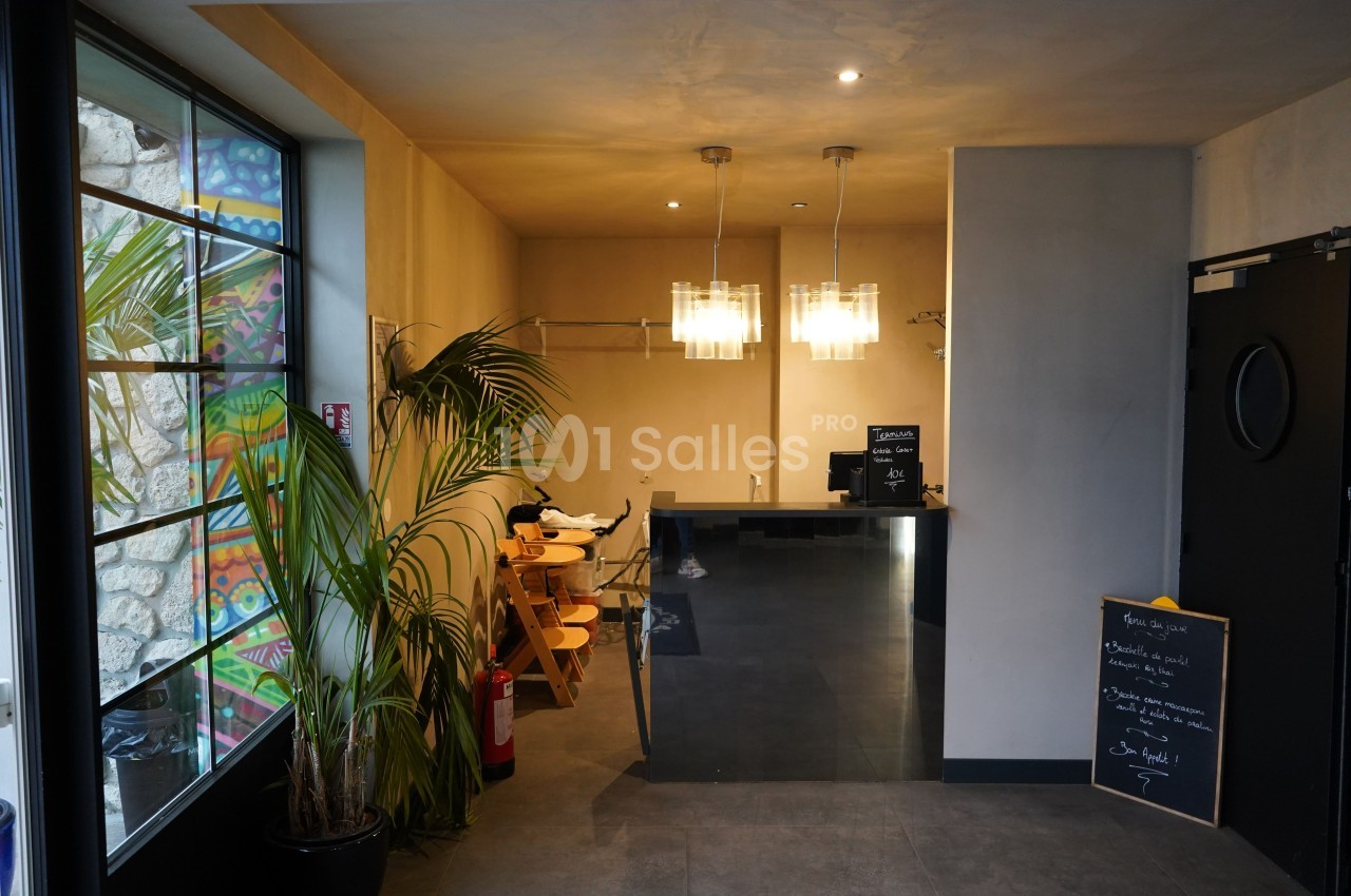 Vue d'un espace intérieur avec un comptoir moderne, des plantes, des chaises en bois et une ardoise d'informations.