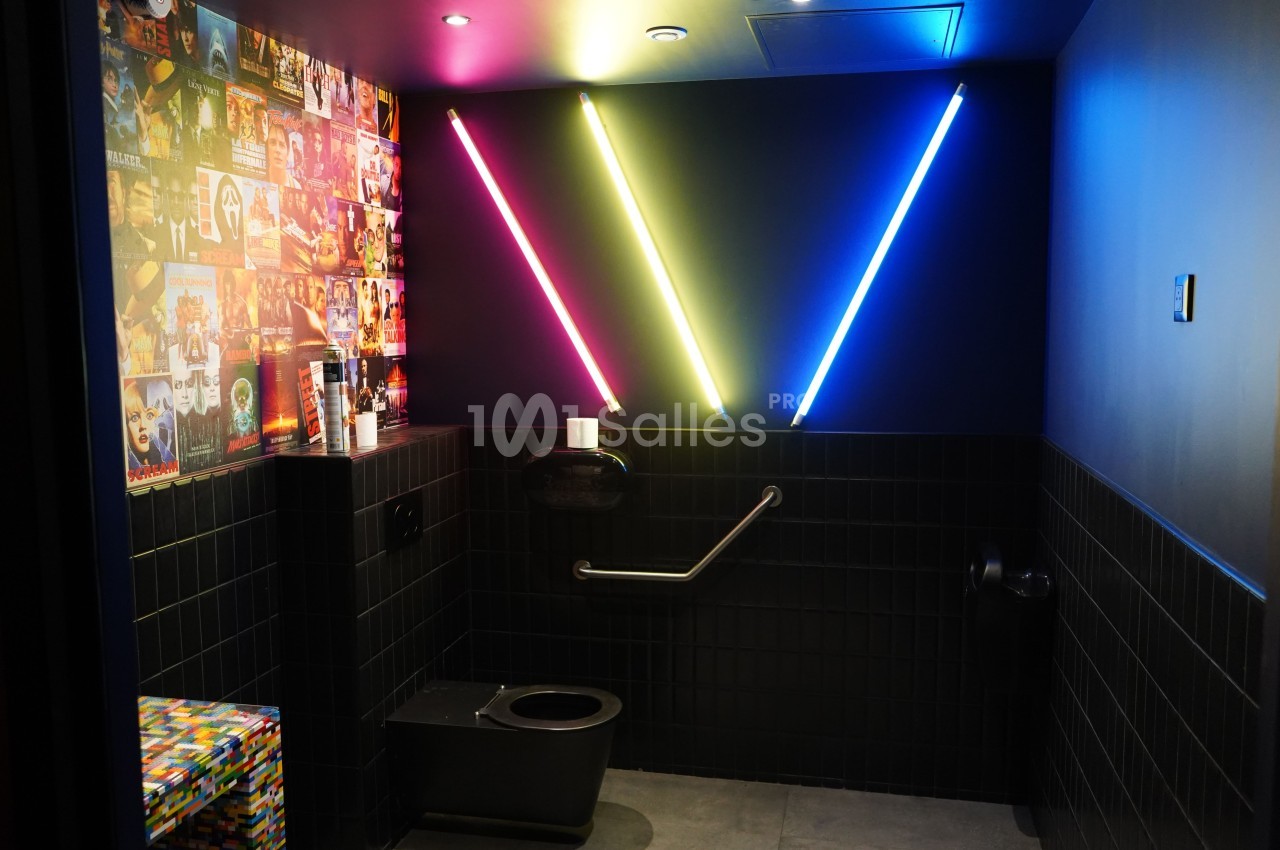 Toilettes modernes avec murs sombres, néons colorés en forme de V et décorations murales de pochettes d'albums.