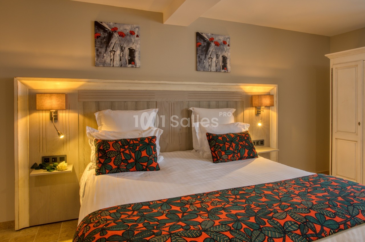 Lit double avec tête de lit en bois, coussins et couvre-lit à motifs colorés, éclairé par des lampes murales.