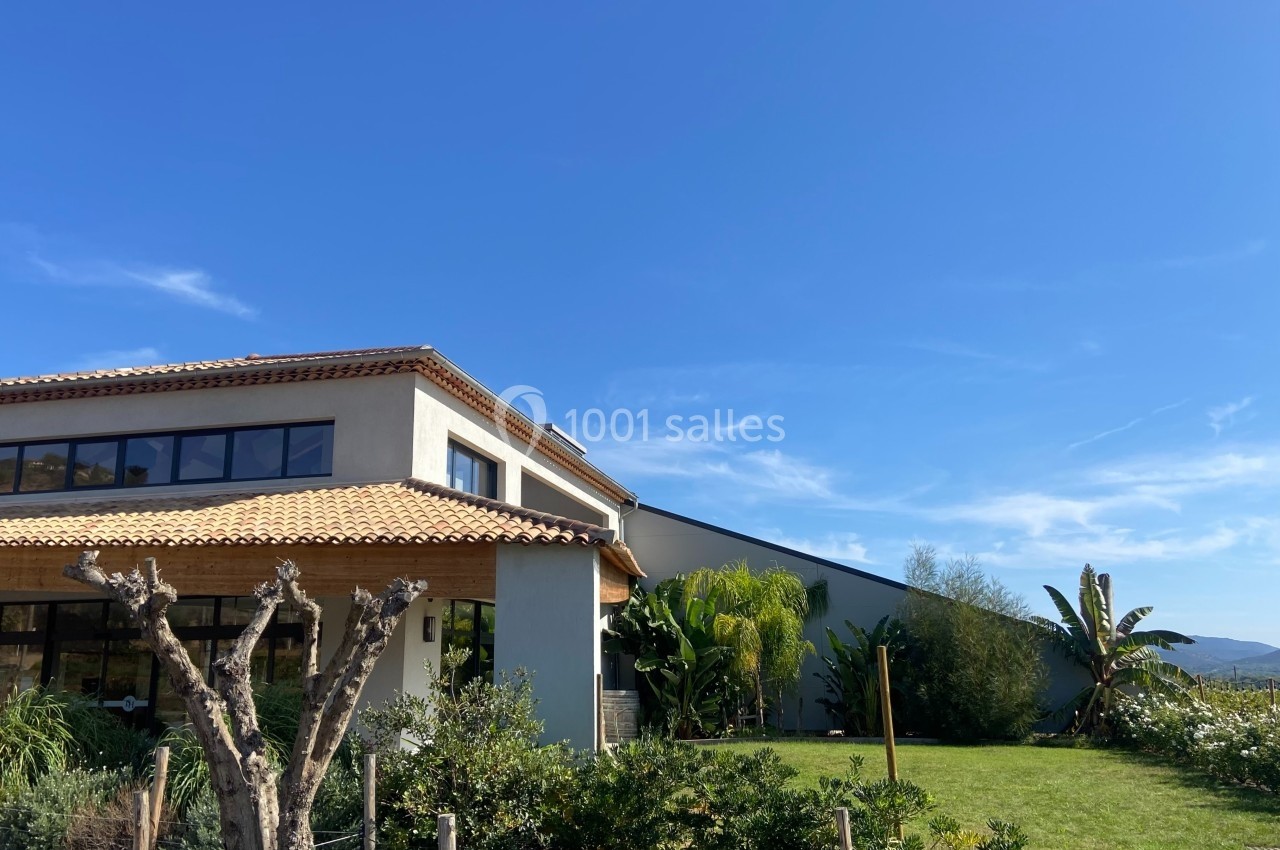 Maison moderne avec toit en tuiles, jardin arboré et ciel bleu dégagé en arrière-plan.