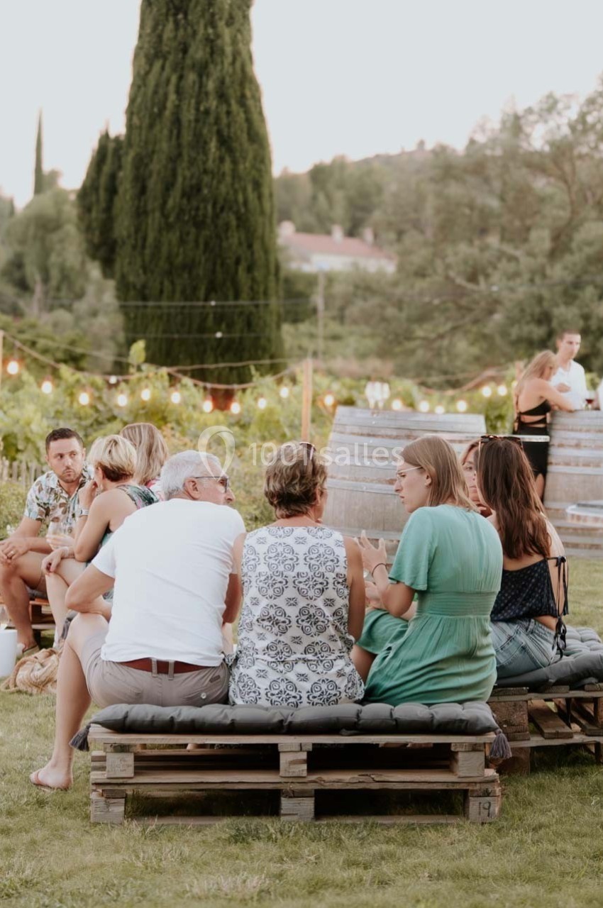 Des personnes discutent assises sur des bancs en palettes dans un jardin, entourées de guirlandes lumineuses.