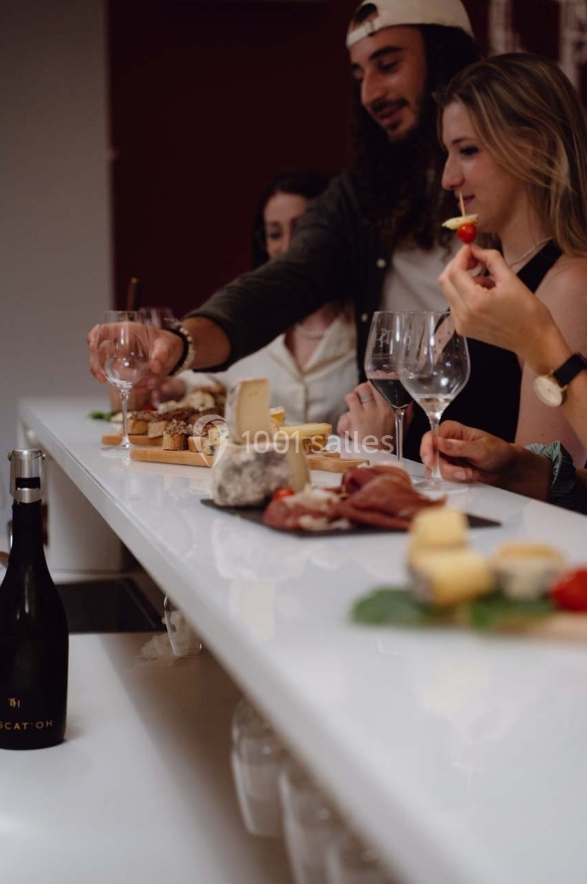Des personnes dégustent du vin et des fromages autour d'un comptoir blanc, avec une bouteille posée au premier plan.