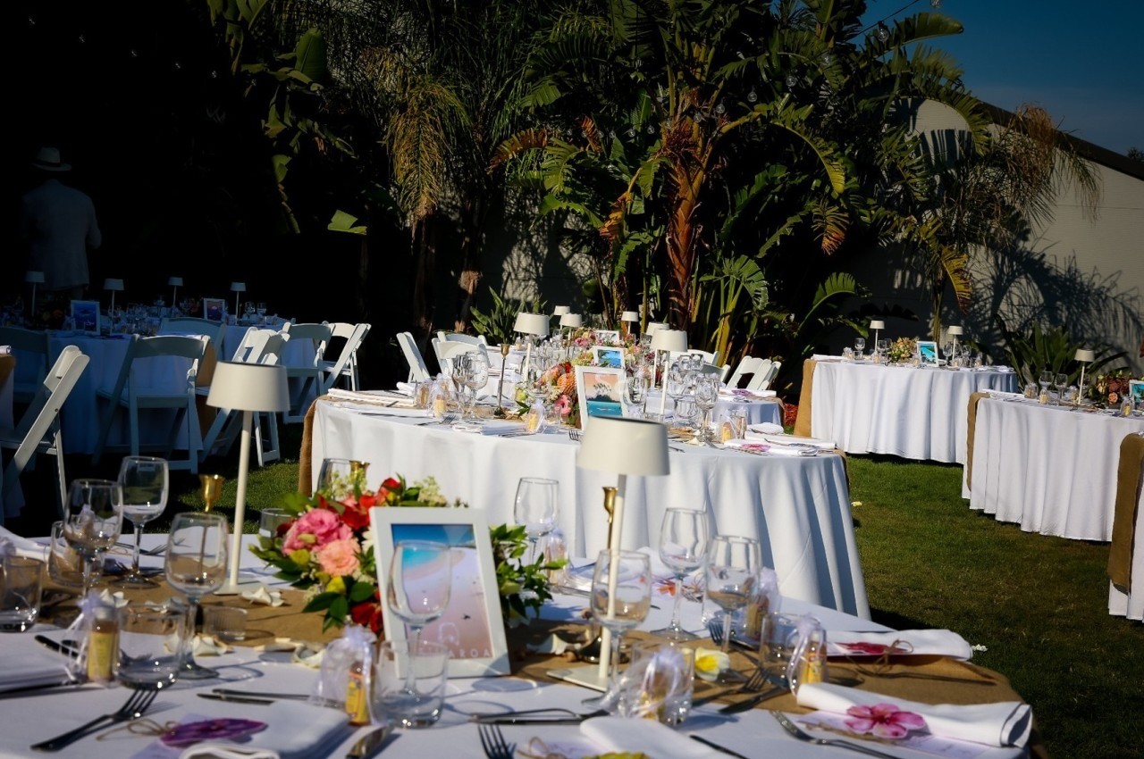 Tables rondes décorées pour un événement en extérieur, avec nappes blanches, fleurs et vaisselle élégante.