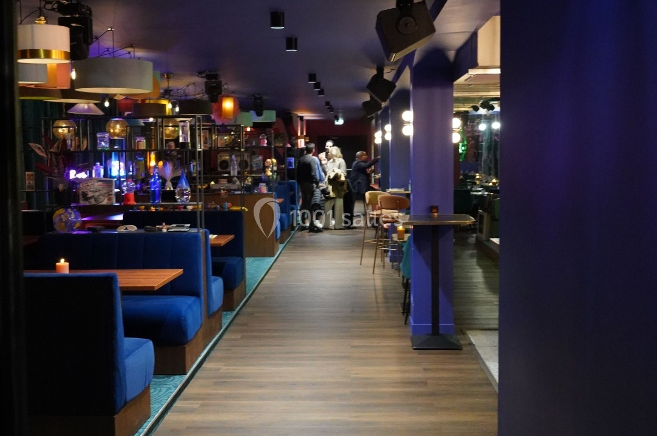 Salle de restaurant moderne avec banquettes bleues, éclairage tamisé et quelques personnes au fond de la pièce.