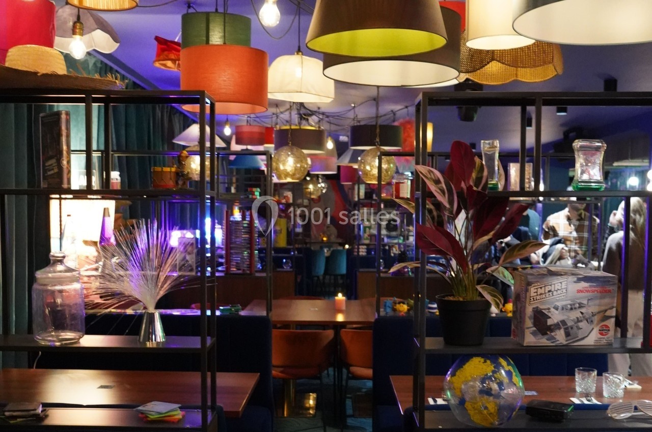 Salle de restaurant colorée avec des étagères décoratives, des plantes, des lampes suspendues et des tables en bois.