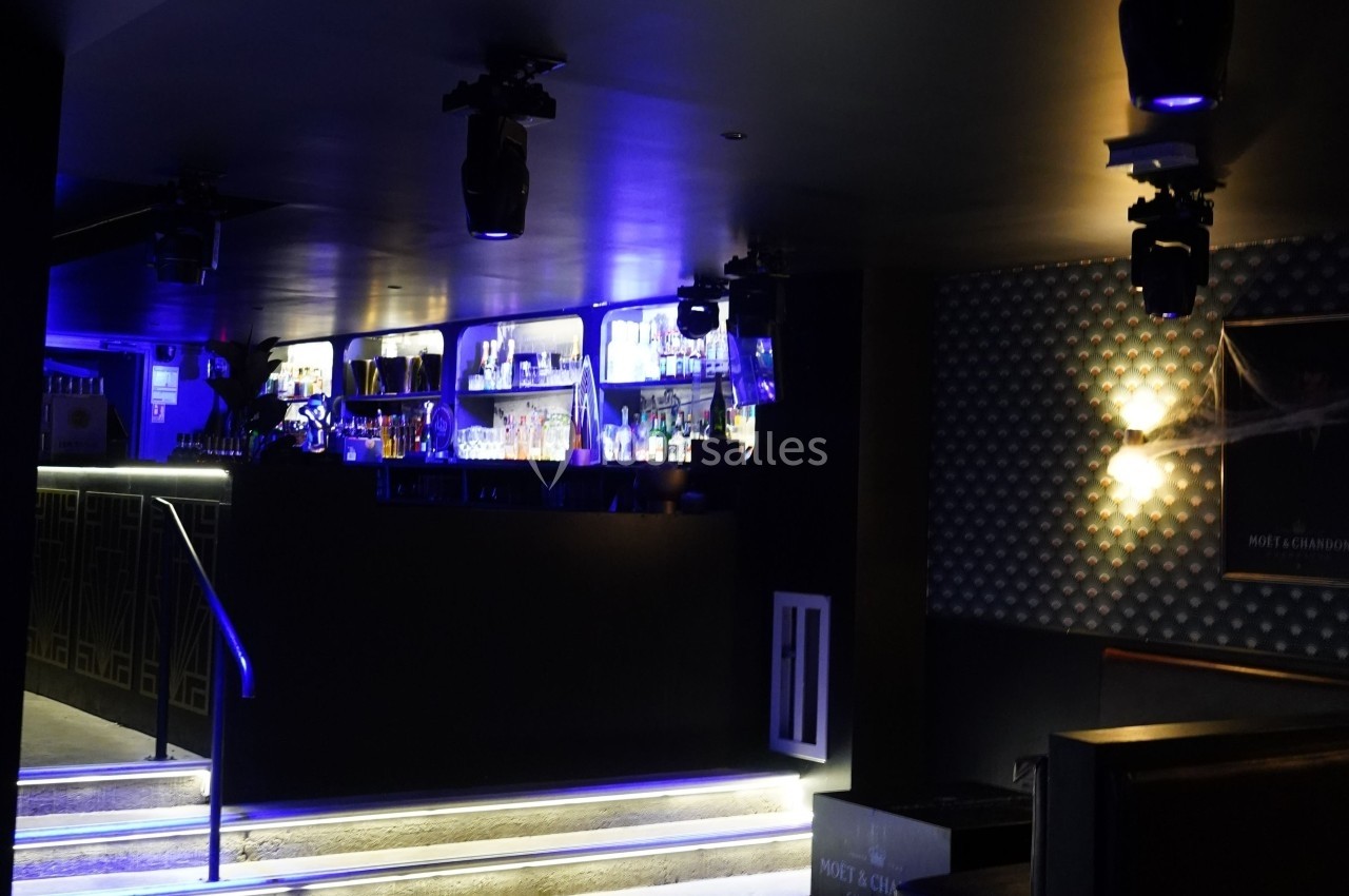Bar moderne avec éclairage bleu, étagères remplies de bouteilles et ambiance tamisée.