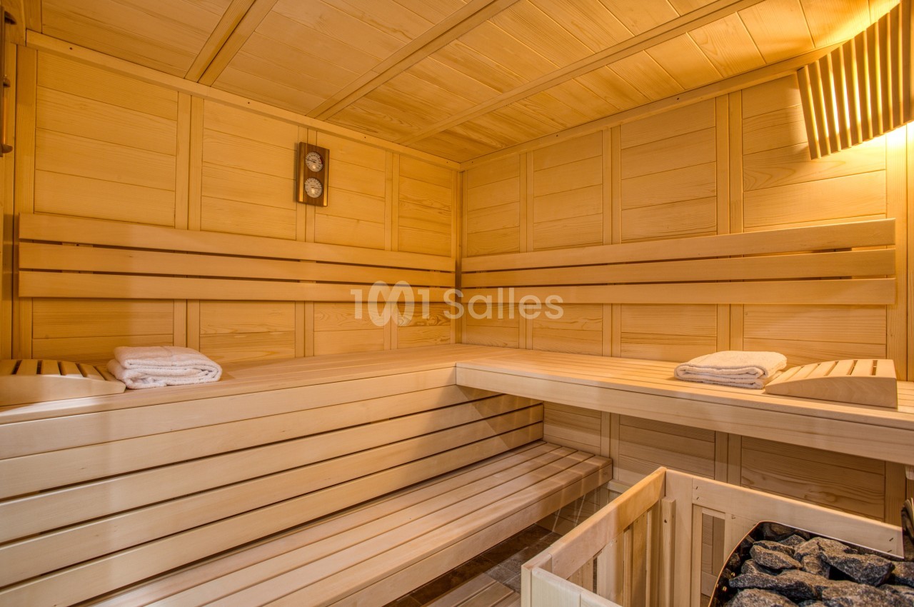 Intérieur d'un sauna en bois clair avec bancs, pierres de chauffage et serviettes pliées.