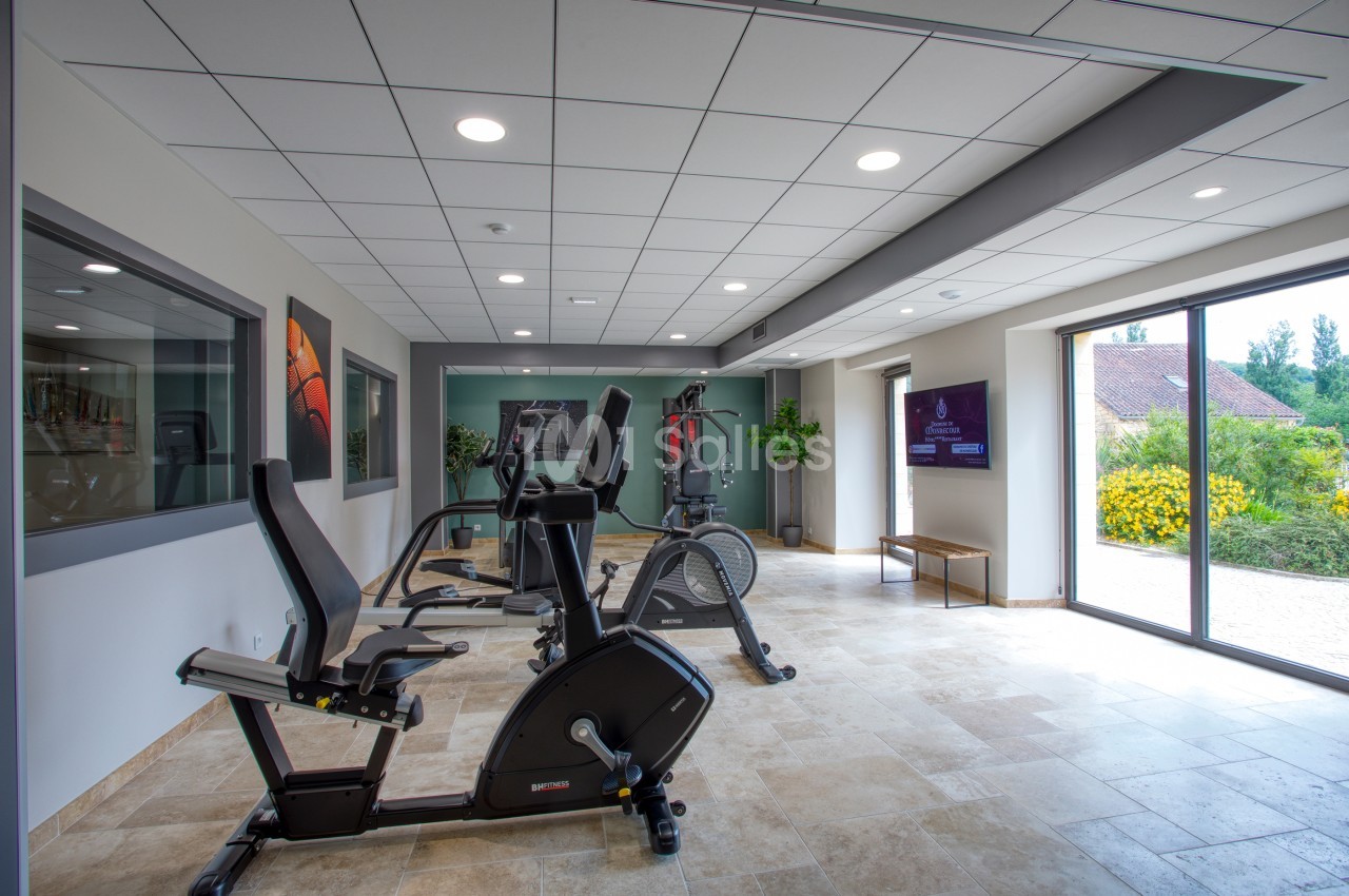Salle de sport lumineuse avec vélos d'exercice, tapis de course et vue sur l'extérieur par une grande baie vitrée.