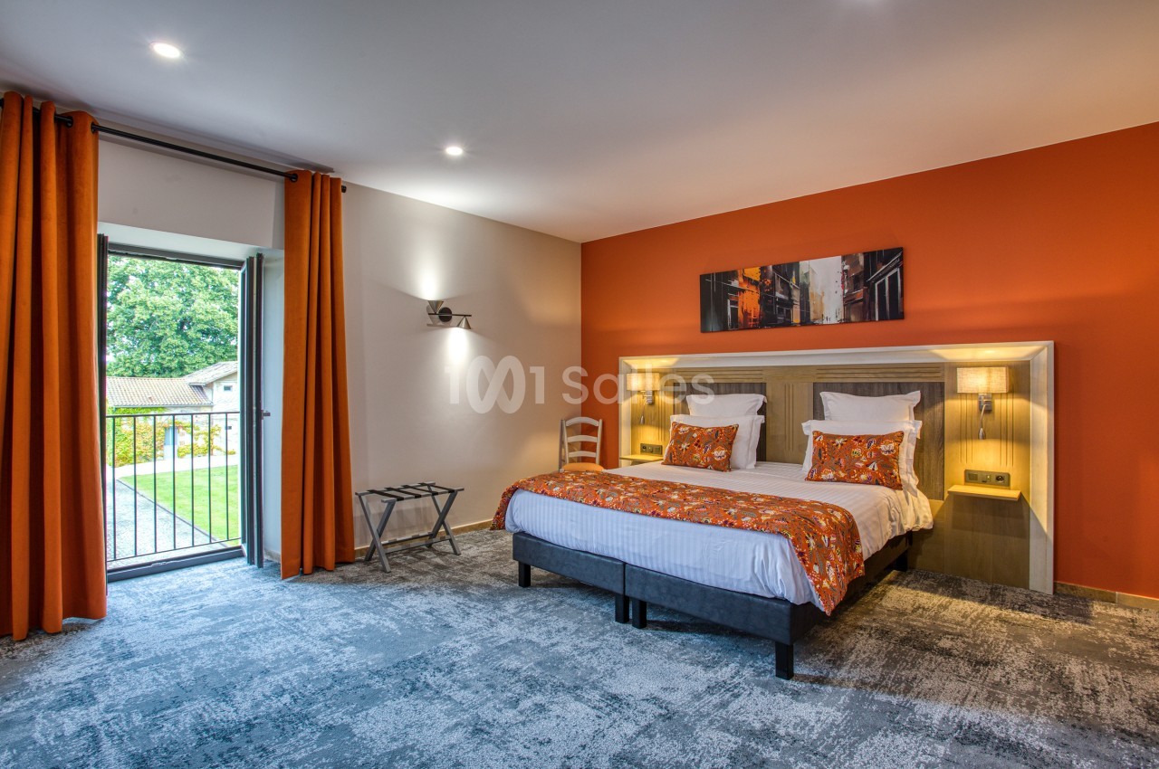 Chambre d'hôtel lumineuse avec un lit double, des rideaux orange, un balcon ouvert et une décoration murale.