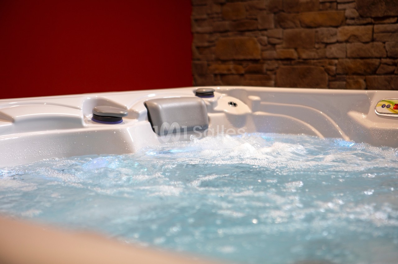 Bain à remous en fonctionnement avec eau bouillonnante, entouré d'un mur en pierre et d'un mur rouge.