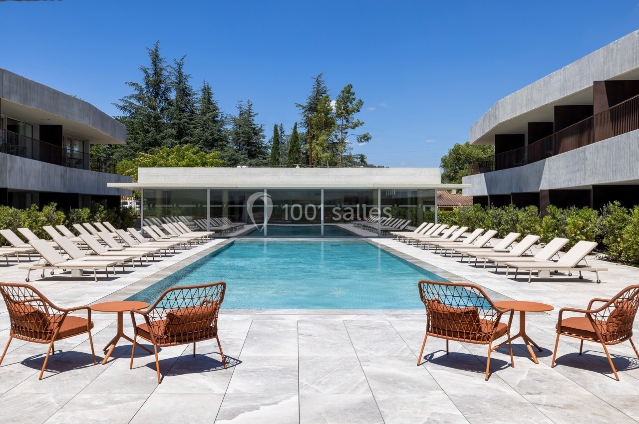 Piscine extérieure entourée de chaises longues et de bâtiments modernes, avec ciel dégagé en arrière-plan.