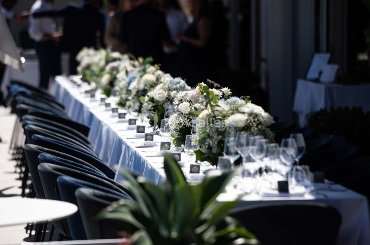 Table dressée pour un événement, ornée de fleurs blanches et de verres, disposée en extérieur sous une lumière naturelle.