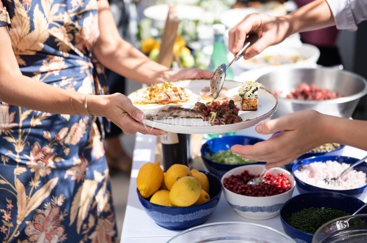 Une personne sert de la nourriture sur une assiette lors d'un buffet avec des bols de garnitures variées.