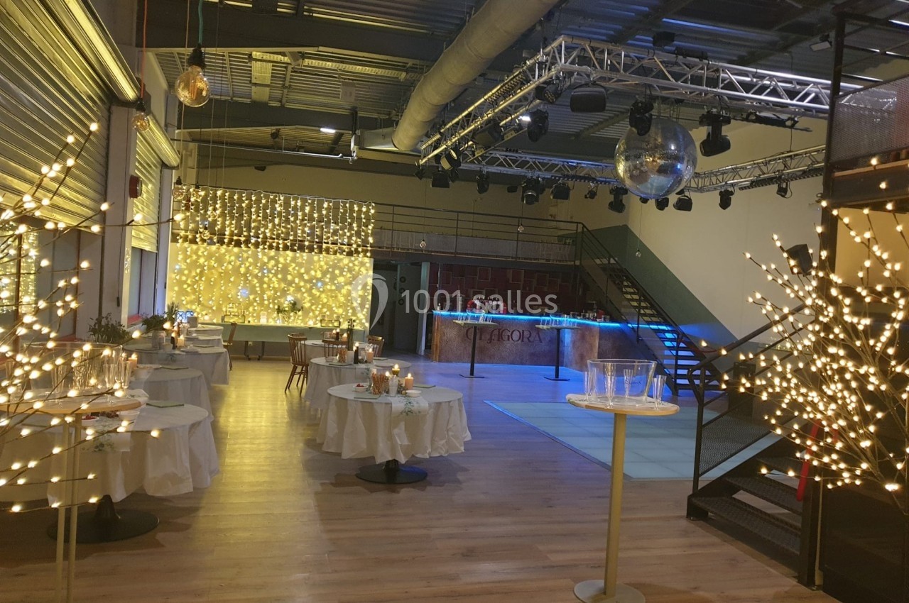 Salle de réception décorée avec des guirlandes lumineuses, tables dressées et piste de danse éclairée.