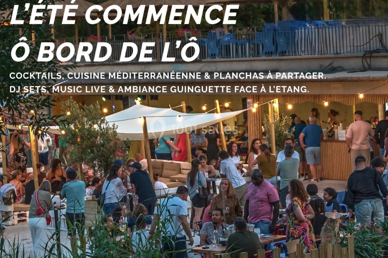 Groupe de personnes profitant d'une soirée animée en terrasse avec éclairage chaleureux et vue sur un étang.