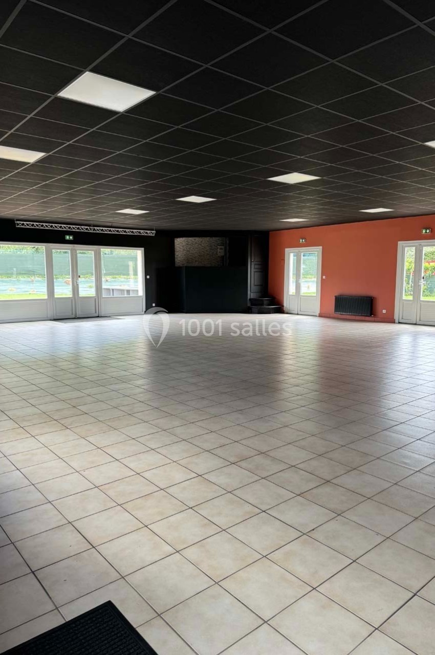 Salle vide avec carrelage clair, murs noirs et rouges, plafond sombre et grandes fenêtres laissant entrer la lumière.
