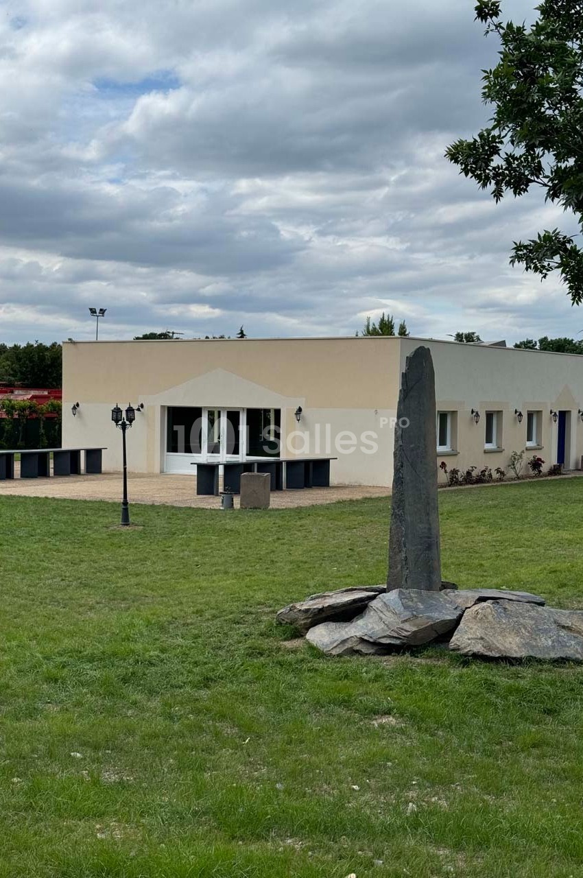 Bâtiment moderne de plain-pied entouré de pelouse, avec une sculpture en pierre au premier plan.