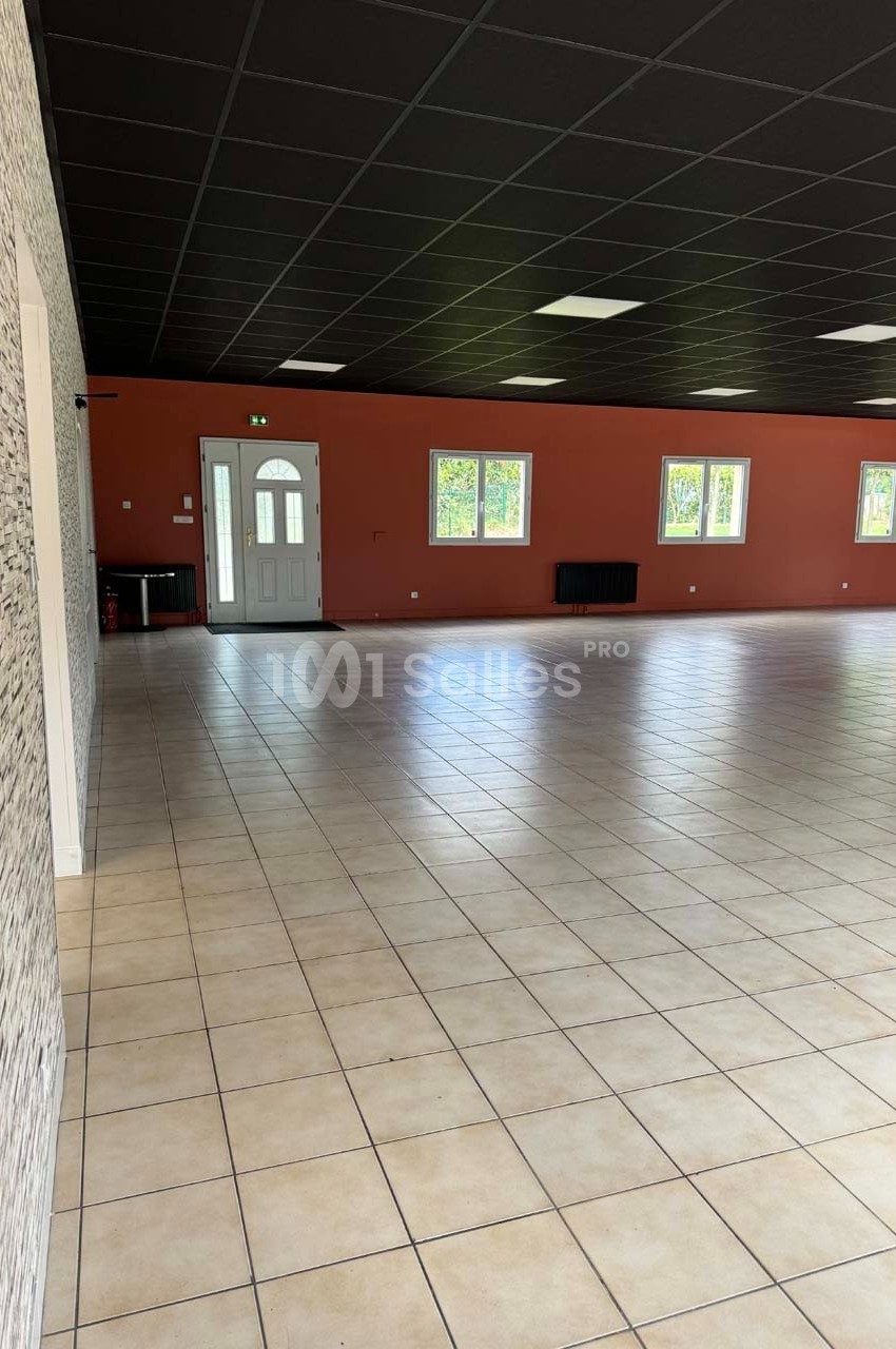 Salle vide avec carrelage beige, murs rouges et blancs, plafond noir, fenêtres alignées et porte d'entrée vitrée.