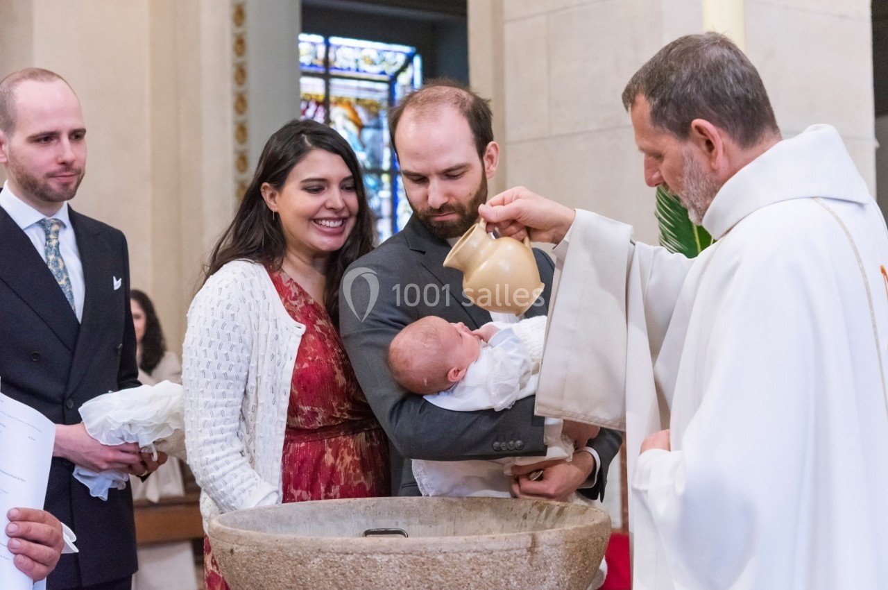Un prêtre verse de l'eau sur le front d'un bébé lors d'un baptême, entouré de ses parents et d'un témoin.