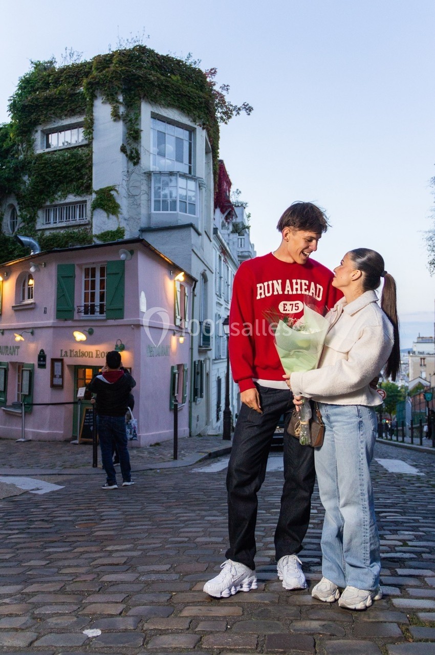 Un couple souriant se tient sur une rue pavée devant des bâtiments colorés et couverts de végétation.