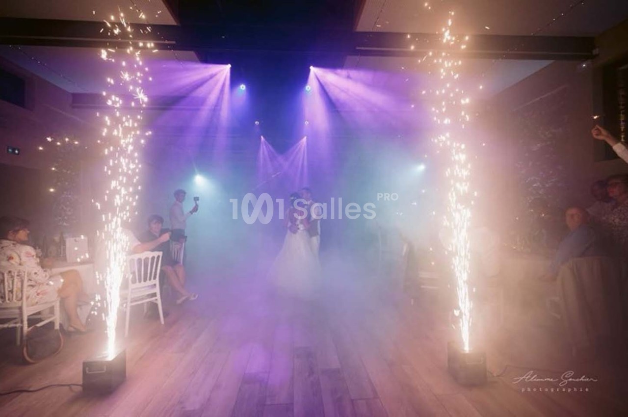 Un couple danse au centre d'une salle éclairée par des projecteurs violets, entouré de jets d'étincelles et de fumée.
